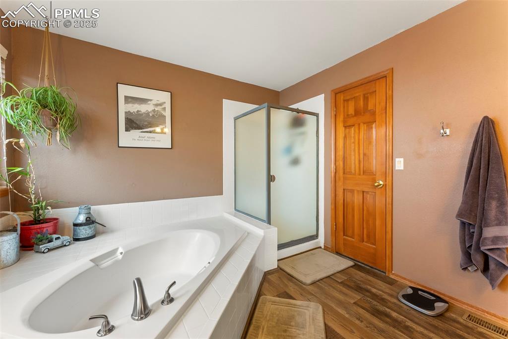 Image 29 of 50: Full bathroom with a shower stall, a garden tub, and dark wood-style floori