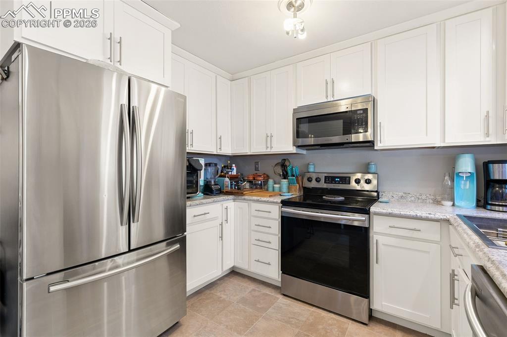 Image 15 of 38: Kitchen with stainless steel appliances, white cabinetry, and light stone c