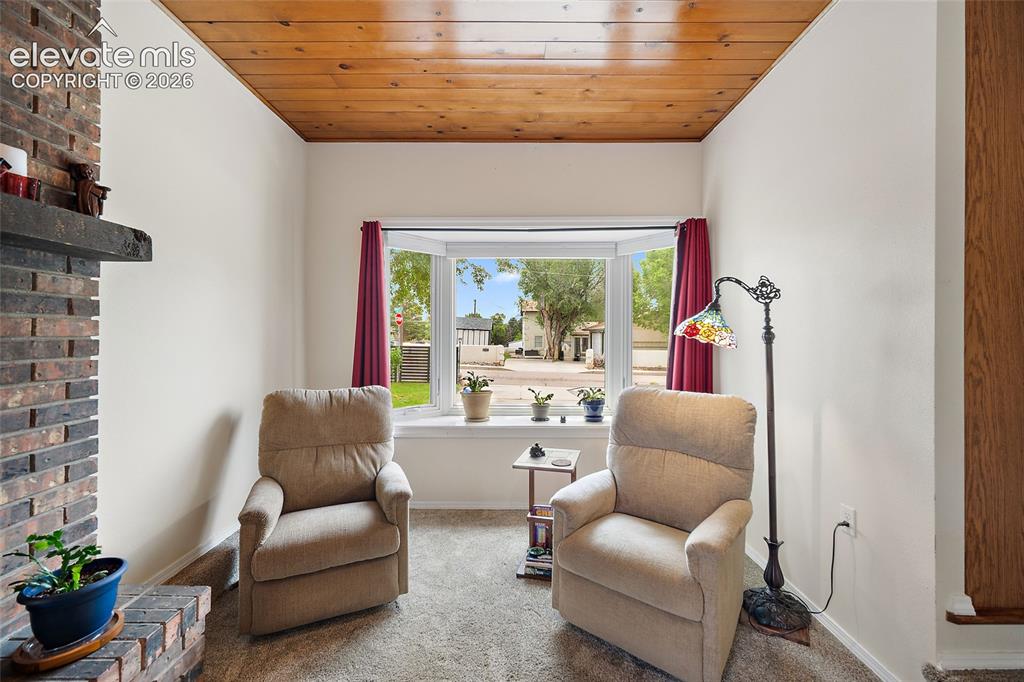 Image 10 of 44: Living area featuring a bay window, wood-paneled ceiling, brick fireplace w