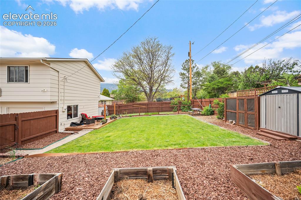 Image 34 of 44: Expansive backyard featuring a manicured lawn, a wooden deck, and a storage