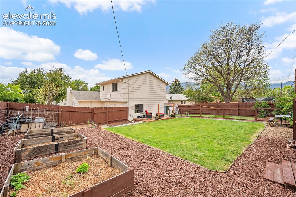 Image 35 of 44: Expansive backyard featuring a lush lawn, multiple raised garden beds, and