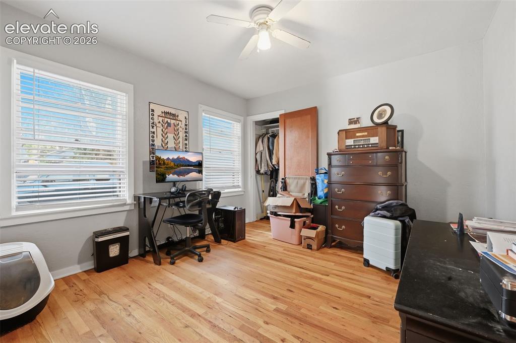 Image 19 of 32: Hardwood flooring throughout, two windows with blinds, ceiling fan with lig