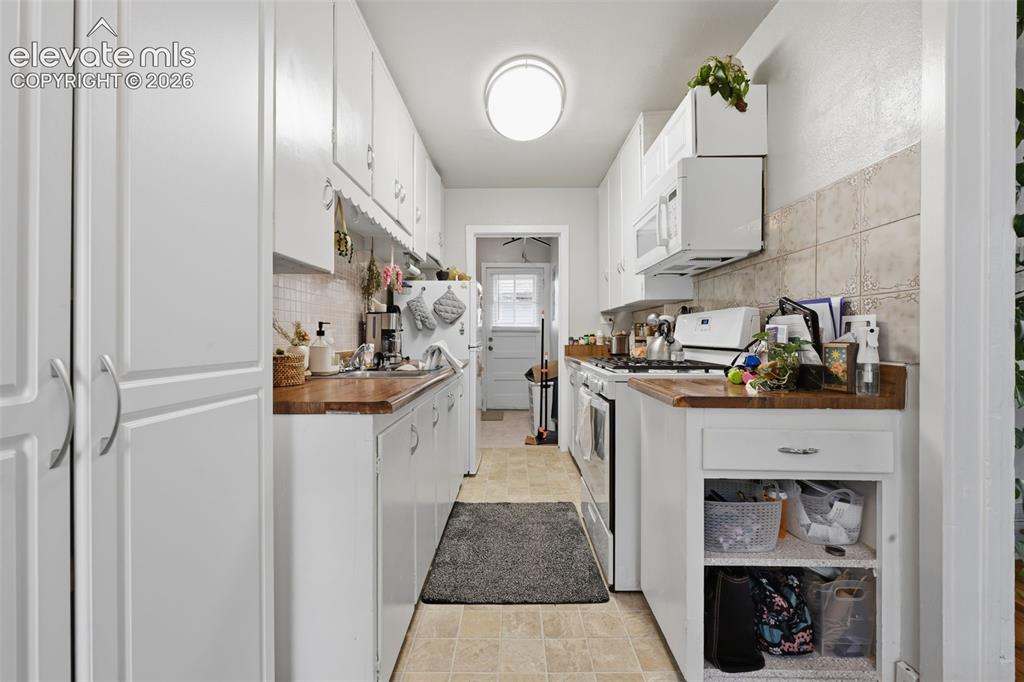 Image 27 of 32: Galley kitchen featuring extensive white cabinetry, wood-finish countertops