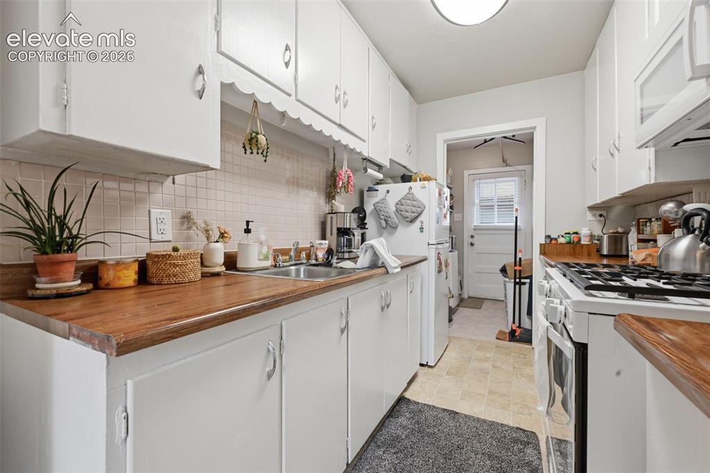 Image 28 of 32: White cabinetry with scallop trim, wood-finish countertops, stainless steel
