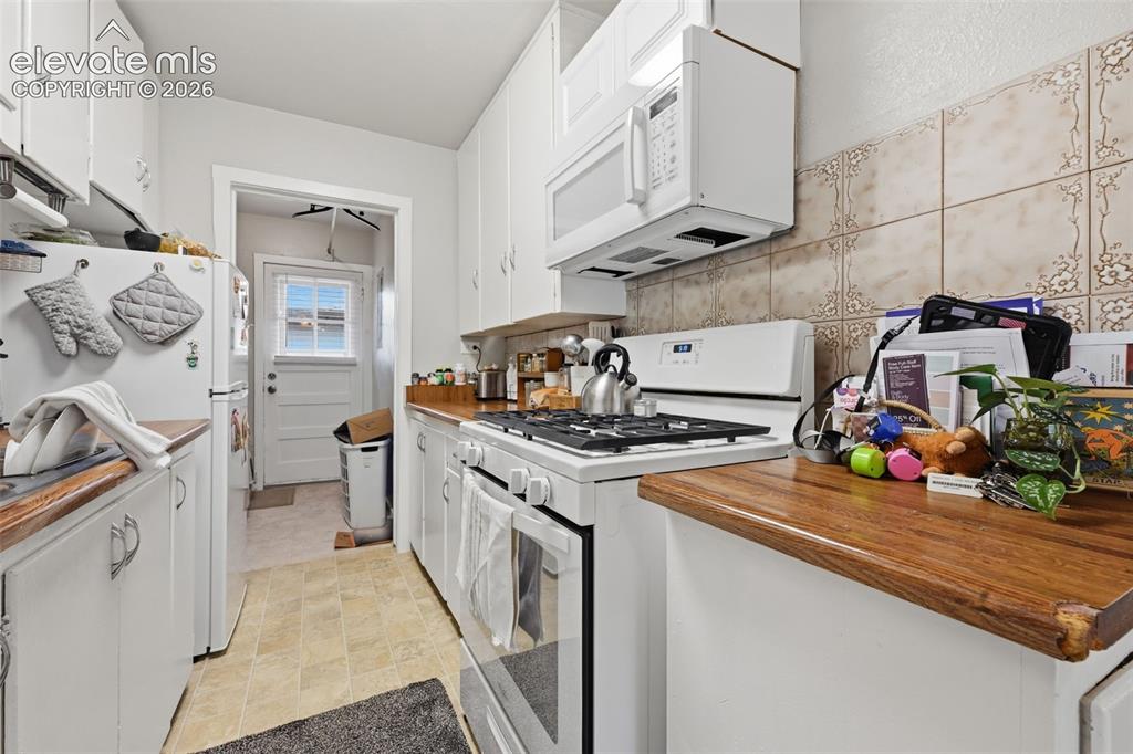 Image 29 of 32: Galley kitchen with white cabinetry, wood-finish countertops, and patterned