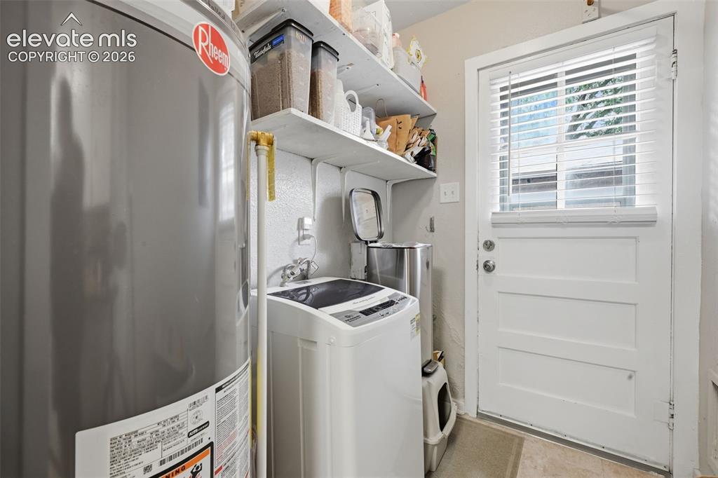 Image 30 of 32: Laundry area featuring built-in shelving and a white panel door with a wind