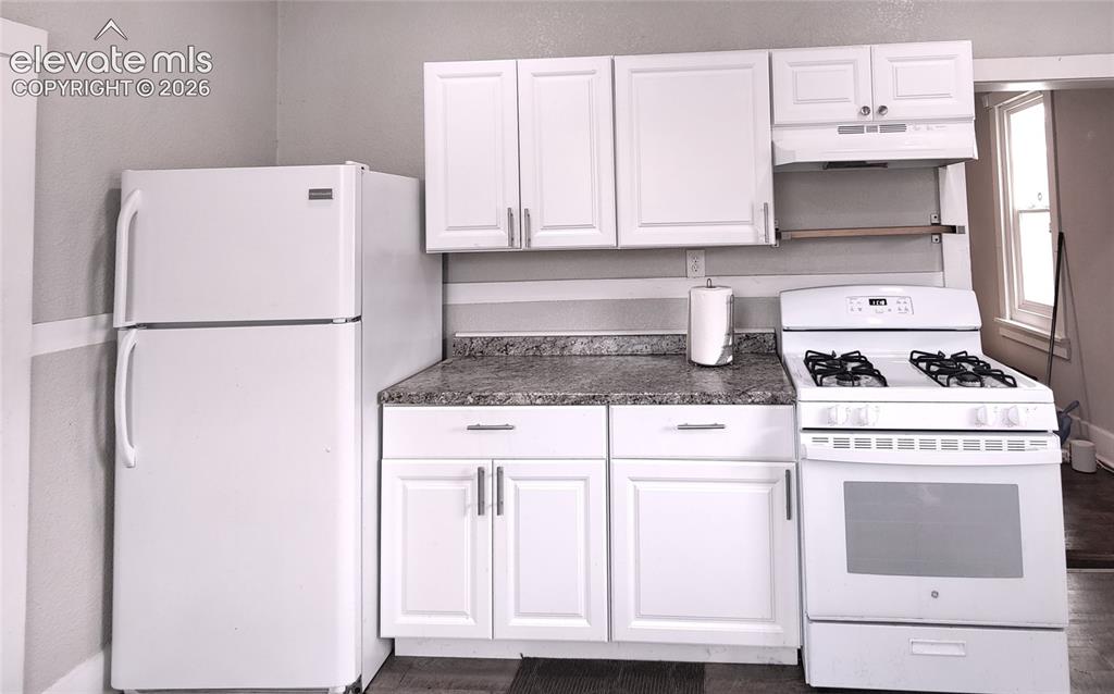 Image 6 of 13: Full kitchen featuring a refrigerator, gas range, white cabinetry, and ston