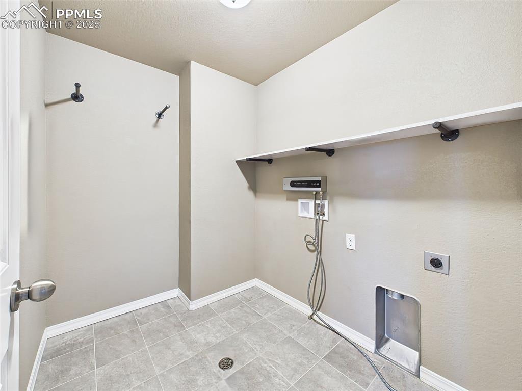 Image 38 of 50: Dedicated laundry space with tile floors, wall-mounted shelf, and washer/dr