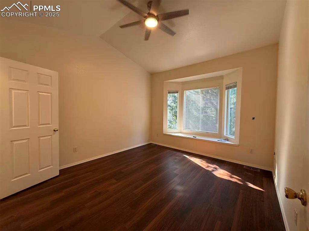 Image 10 of 13: Empty room with dark wood finished floors, vaulted ceiling, and ceiling fan