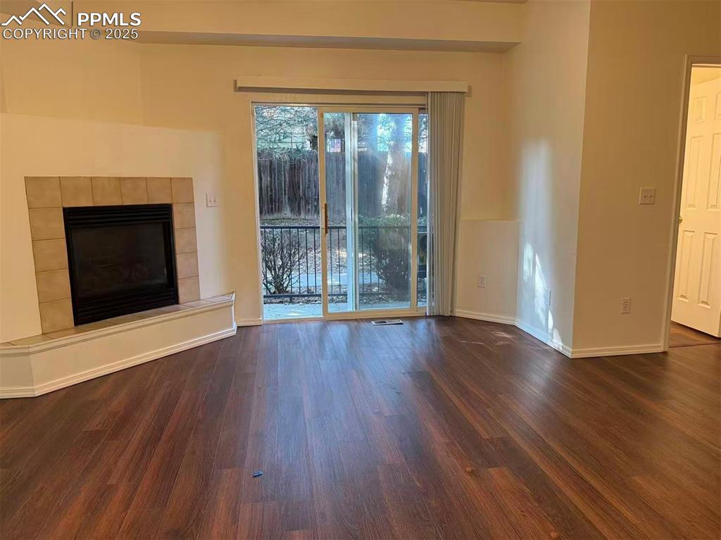 Image 3 of 13: Unfurnished living room with a tile fireplace and dark wood-style flooring