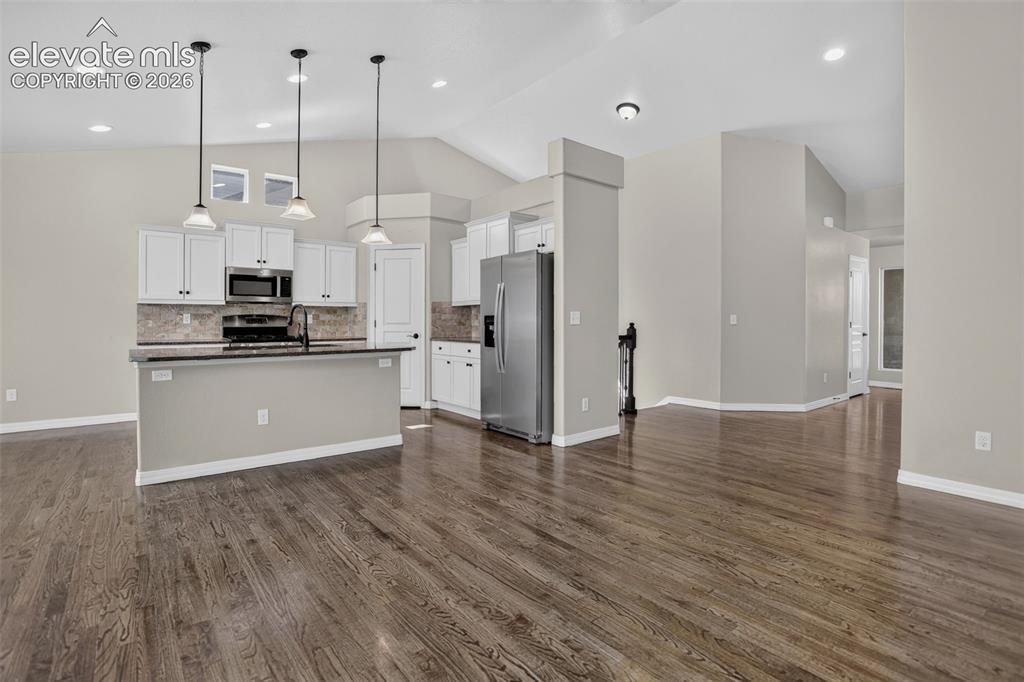 Image 10 of 50: Open-concept living area with wood-finish flooring, vaulted ceilings, and r