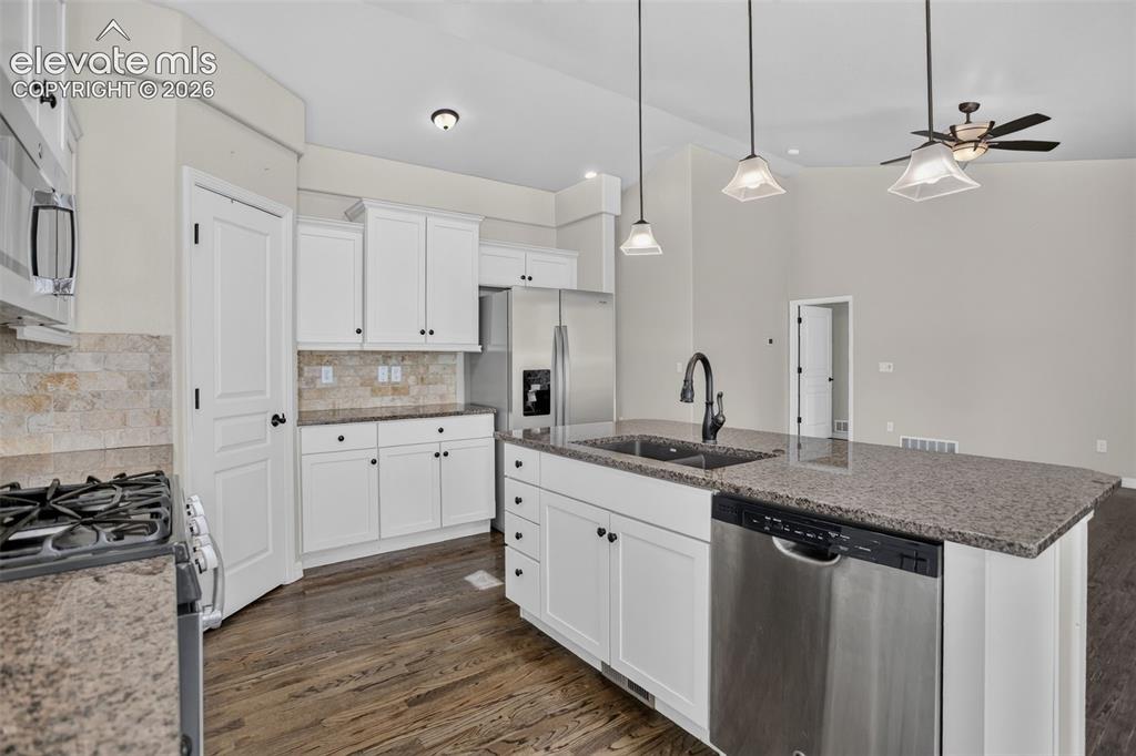 Image 15 of 50: Kitchen featuring dark wood-finish flooring, white cabinetry, a stone-tiled