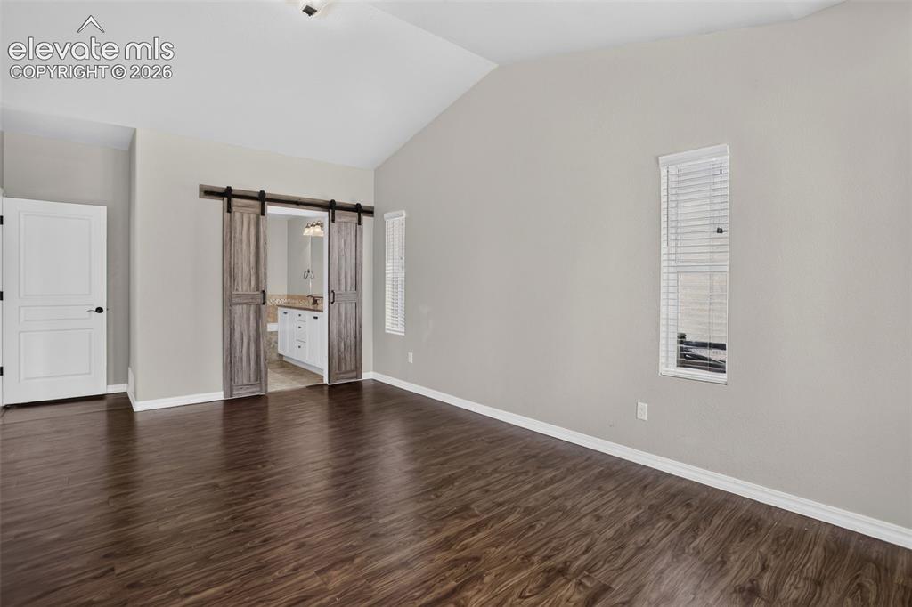 Image 20 of 50: Vaulted ceiling, wood-finish flooring, and a white interior door
