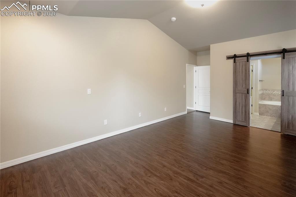 Image 22 of 44: Unfurnished bedroom featuring a barn door, dark wood finished floors, lofte