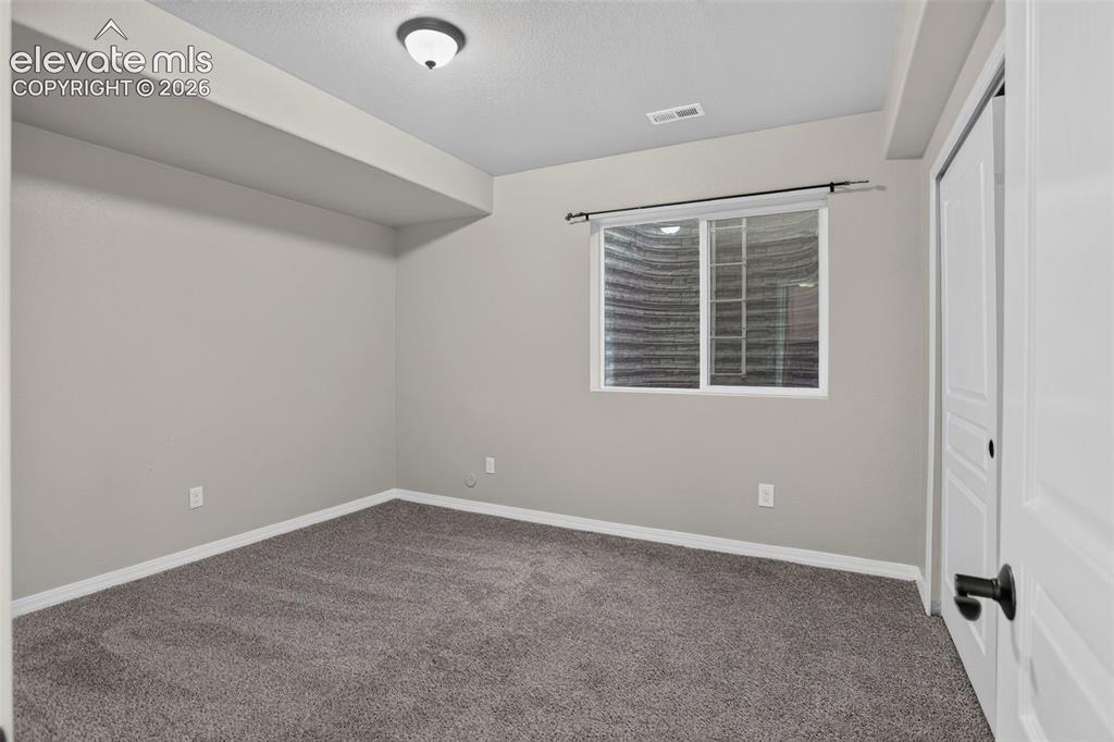 Image 37 of 50: Window with white trim, gray carpet, and a white paneled door with black ha