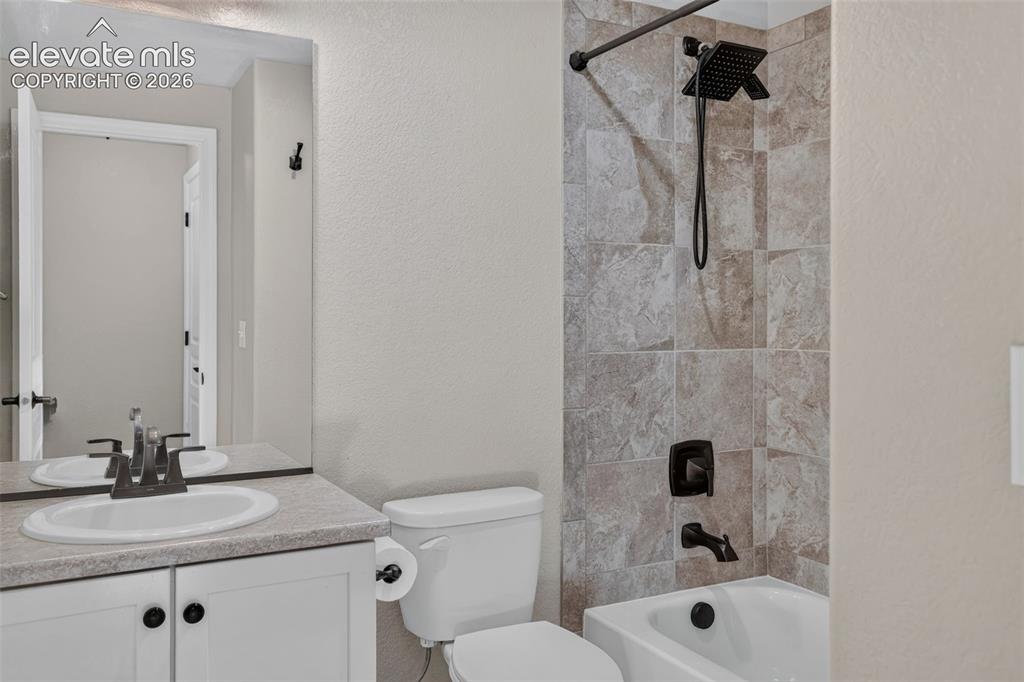 Image 44 of 50: Bathroom featuring a shower-tub combination, tiled shower surround, dark br