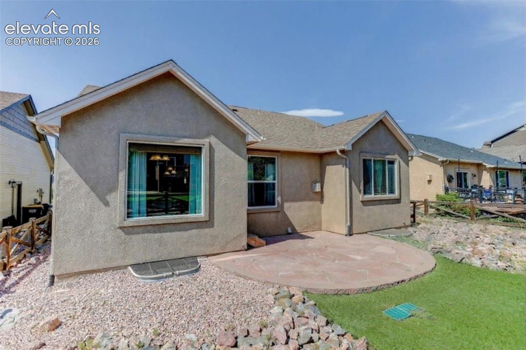 Image 46 of 50: Stucco exterior with a pitched roof, featuring multiple windows, a stone pa