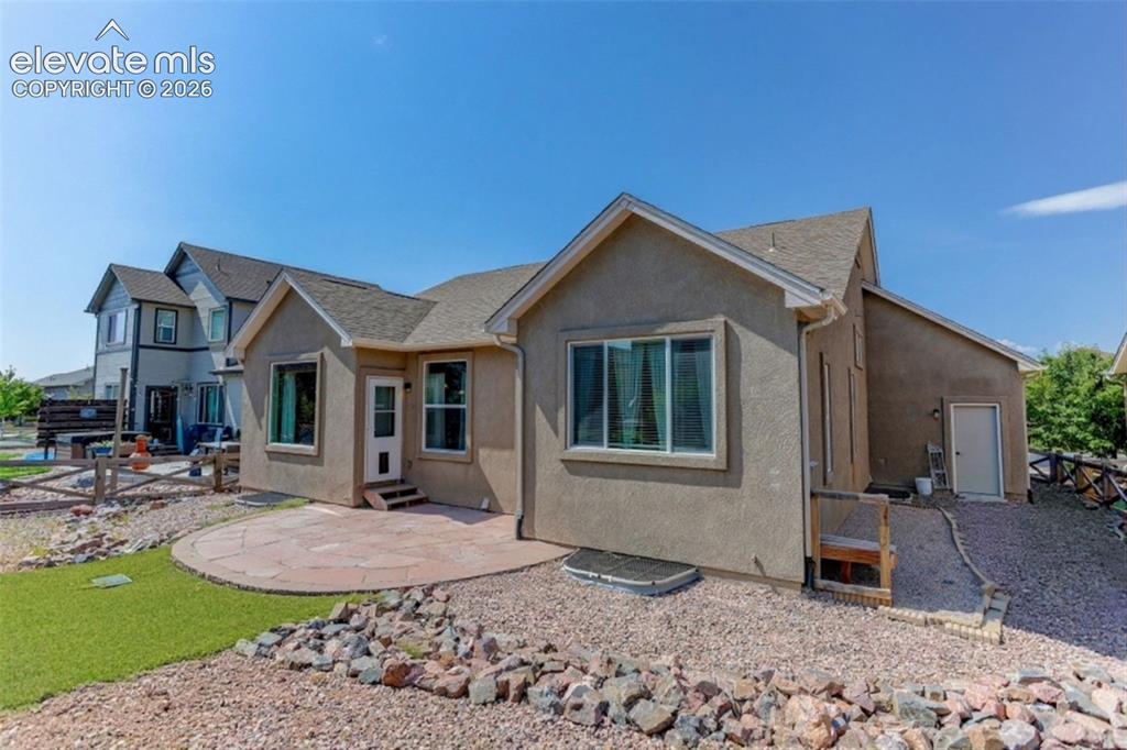 Image 48 of 50: Stucco exterior with multiple windows, a stone patio, and a gravel landscap