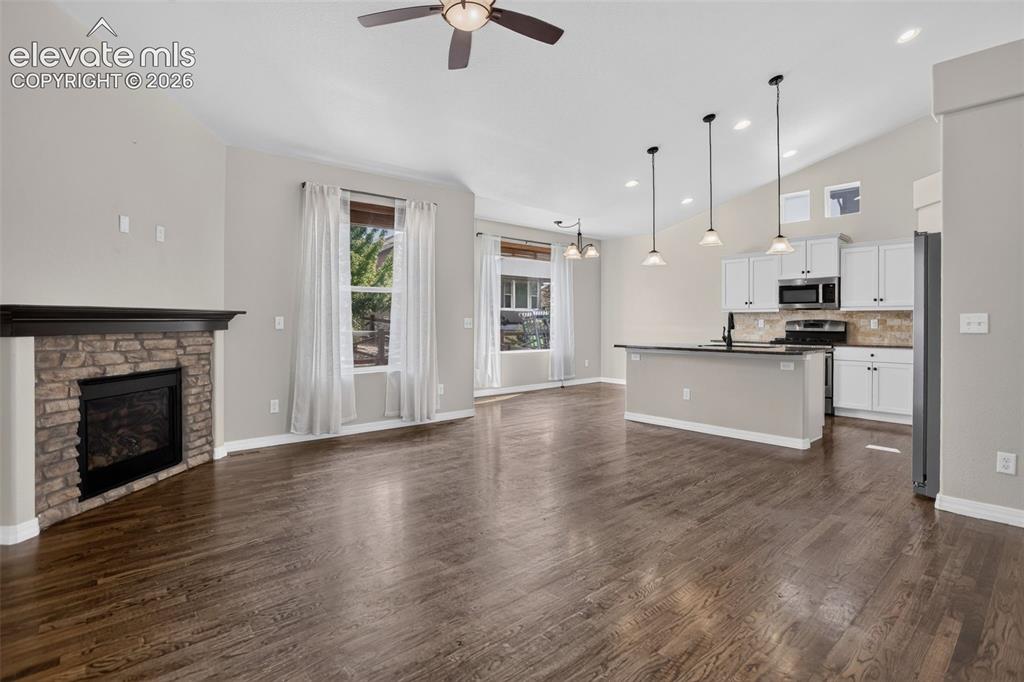 Image 7 of 50: Vaulted ceiling with a ceiling fan, wood-finish flooring, stone-clad firepl