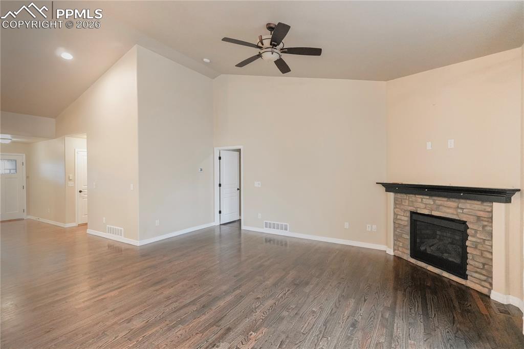 Image 9 of 44: Unfurnished living room with ceiling fan, dark wood-style flooring, a stone