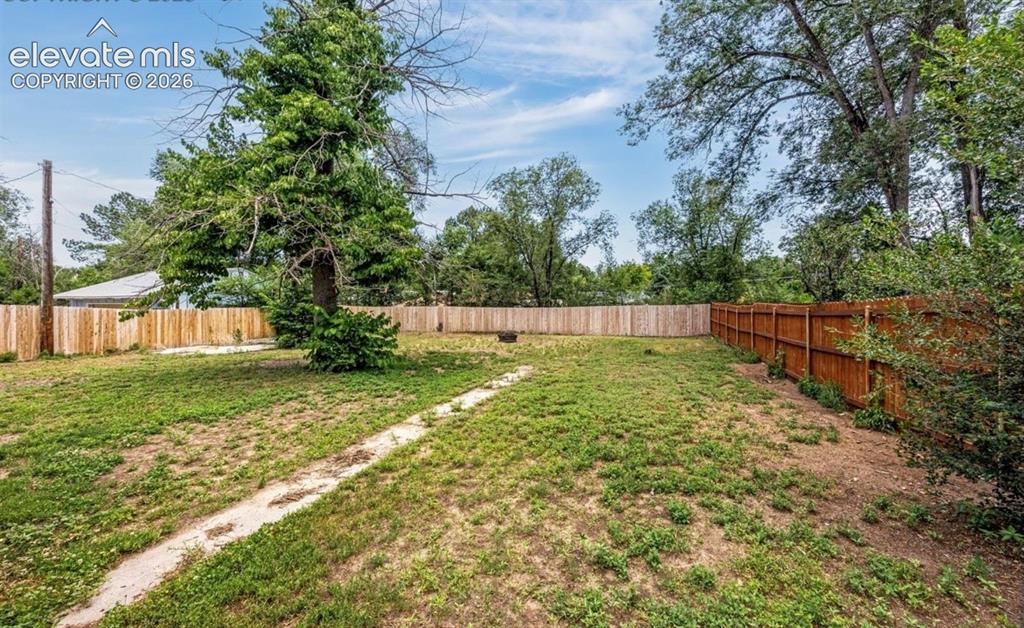 Image 11 of 11: Spacious backyard with mature trees, established lawn, and wooden perimeter