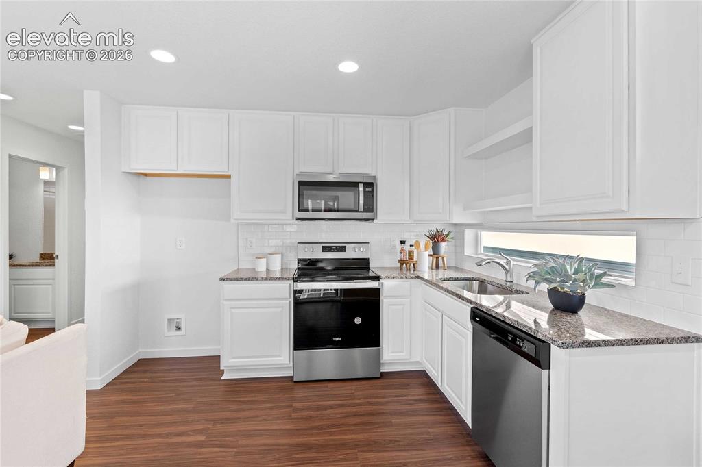 Image 15 of 25: White cabinetry with polished hardware, granite countertops, white subway t