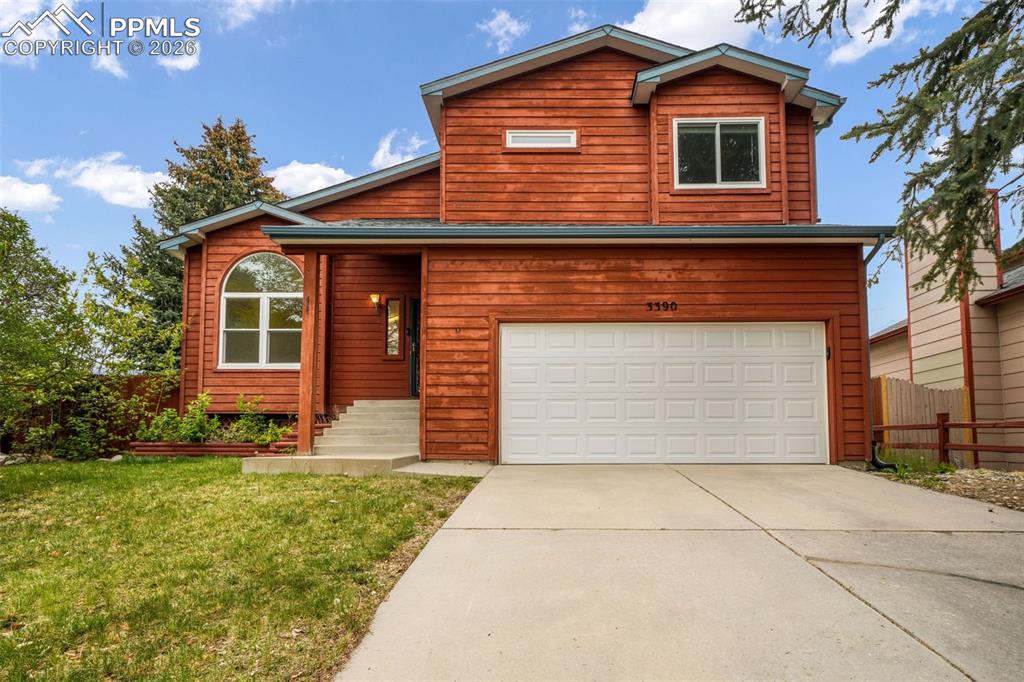 Image 2 of 45: Two-story residence featuring a red wood-panel exterior, an attached two-ca