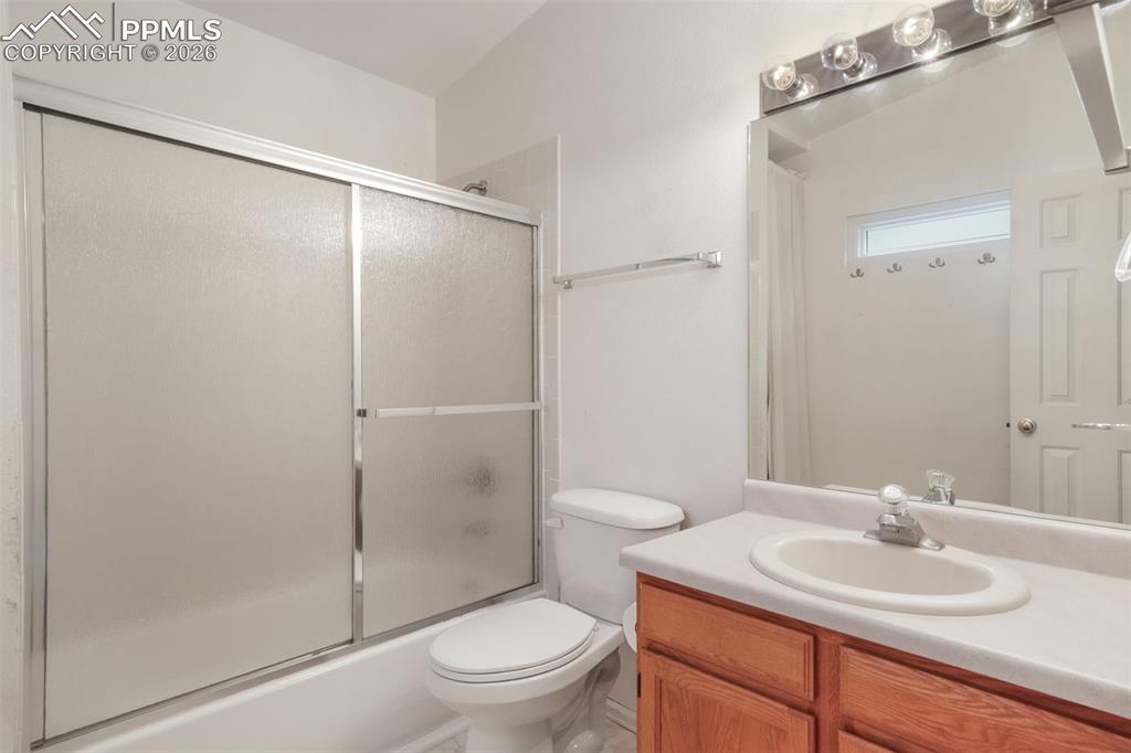 Image 21 of 45: Corner fireplace with white tile surround, ceiling fan, carpet flooring, an