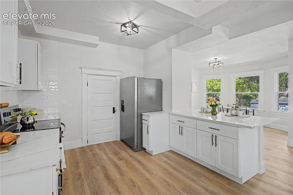 Image 15 of 35: Bright kitchen with wood-finish flooring, white cabinetry, a large kitchen 