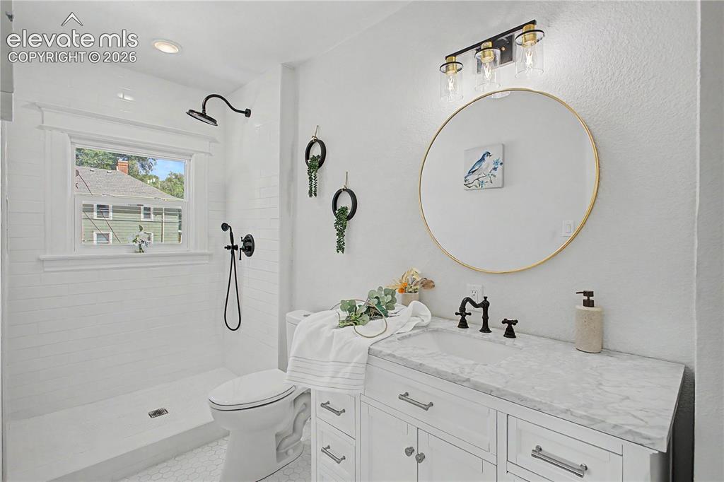 Image 30 of 35: White tile shower with black fixtures and a window