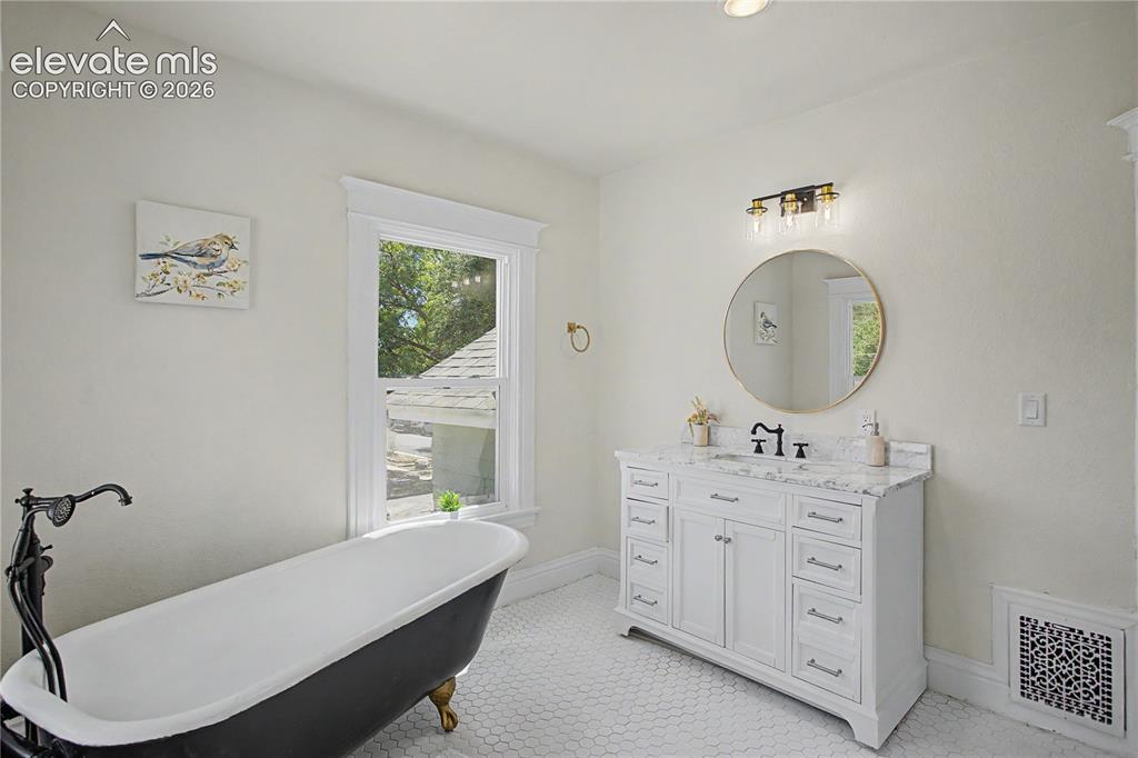 Image 32 of 35: Freestanding clawfoot tub, white hexagonal floor tiling, white vanity with