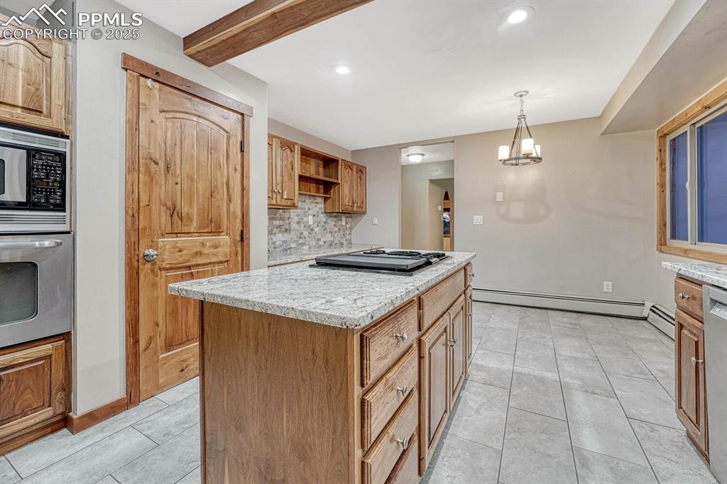 Image 10 of 47: Kitchen featuring baseboard heating, a center island, backsplash, built in