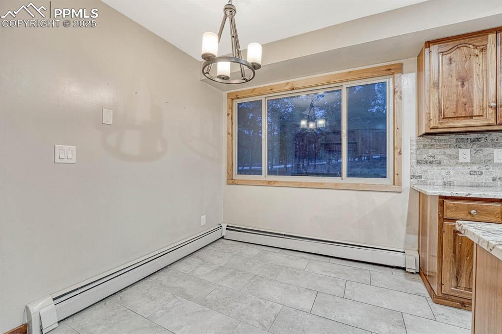 Image 12 of 47: Unfurnished dining area with a baseboard radiator and an inviting chandelie