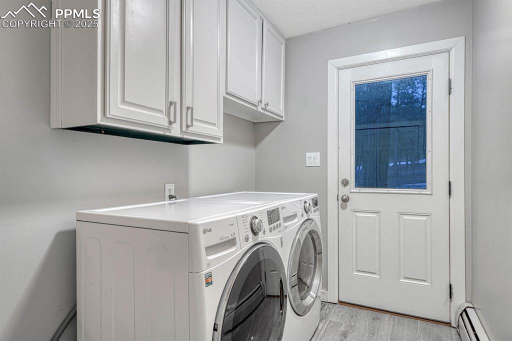 Image 17 of 47: Laundry area with cabinet space, a baseboard radiator, light wood finished