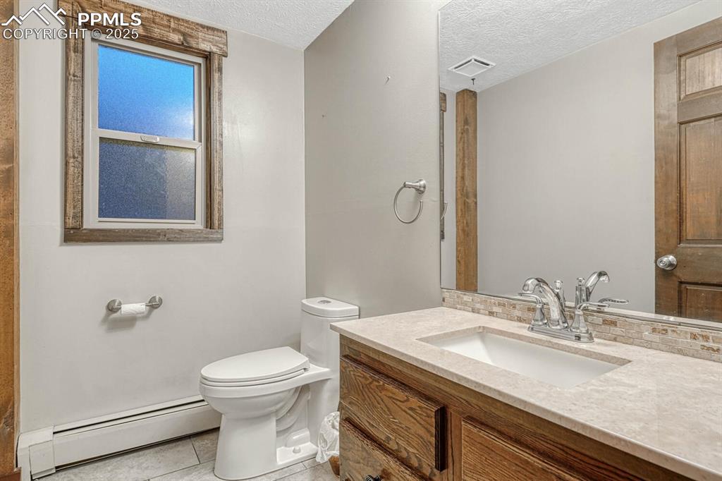 Image 25 of 47: Bathroom with visible vents, toilet, a textured ceiling, baseboard heating,