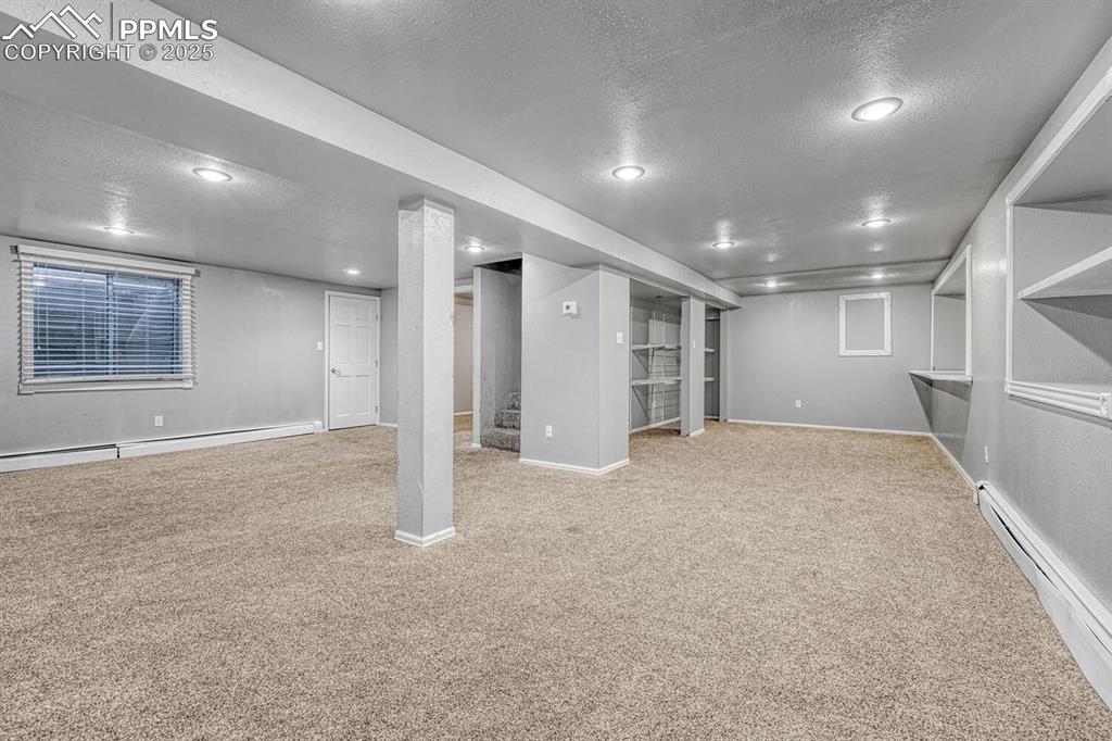 Image 29 of 47: Finished basement with baseboards, baseboard heating, a textured ceiling, r