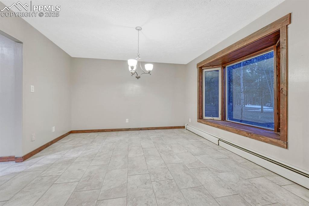 Image 7 of 47: Spare room with a baseboard radiator, a notable chandelier, and baseboards