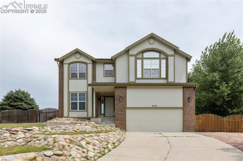 Caption: View of front facade with a gate, brick siding, concrete driveway, and an attached garage