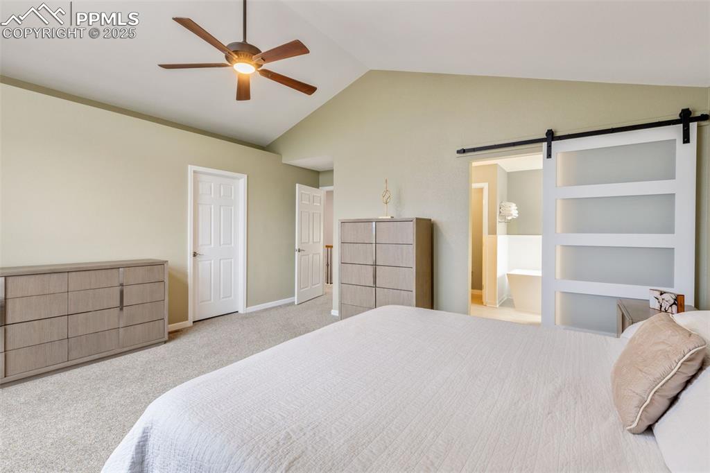 Image 19 of 41: Carpeted bedroom with a barn door, lofted ceiling, and ceiling fan