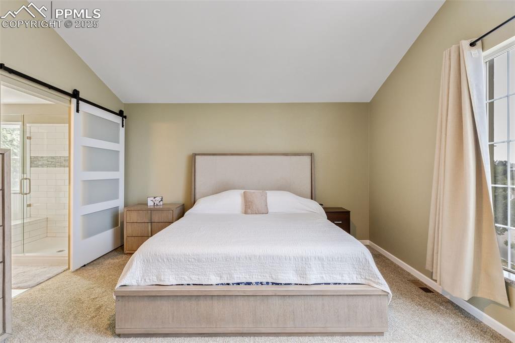Image 20 of 41: Bedroom featuring light carpet, vaulted ceiling, a barn door, and ensuite b