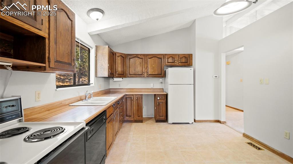 Image 16 of 50: Kitchen featuring white appliances, light countertops, brown cabinetry, and