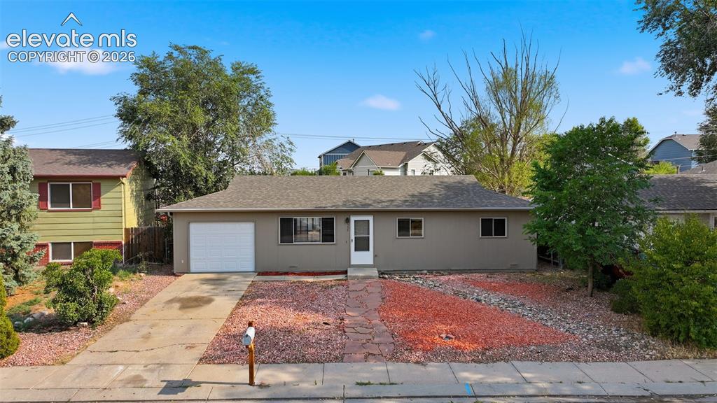 Caption: Attached single-car garage, concrete driveway, and low-maintenance rock landscaping
