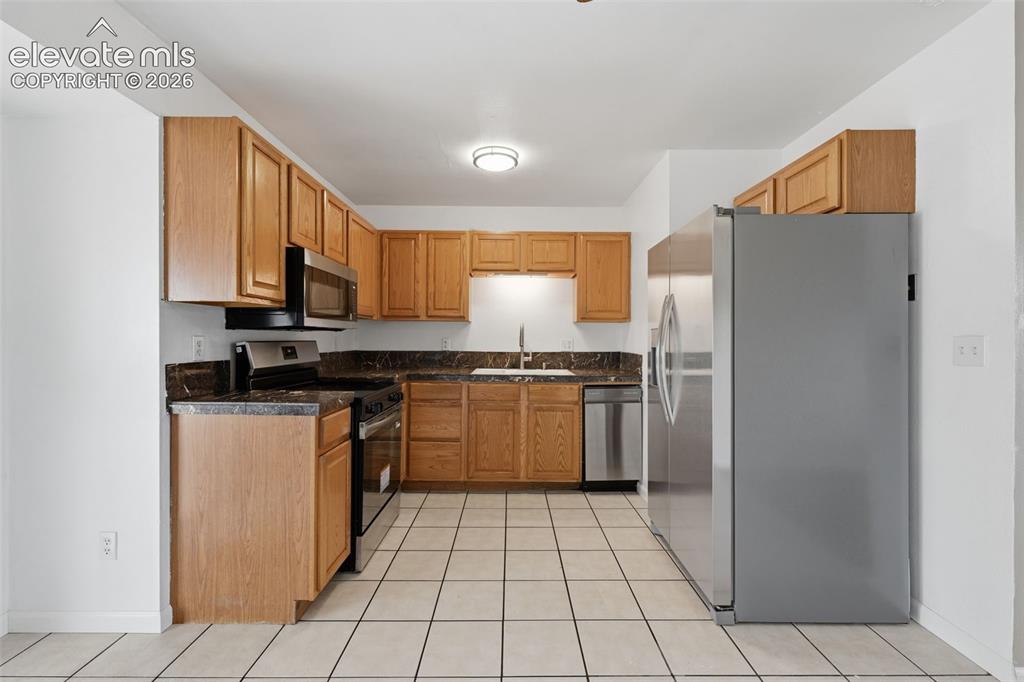Image 21 of 36: Kitchen featuring wood cabinetry, dark countertops, white tile flooring, st