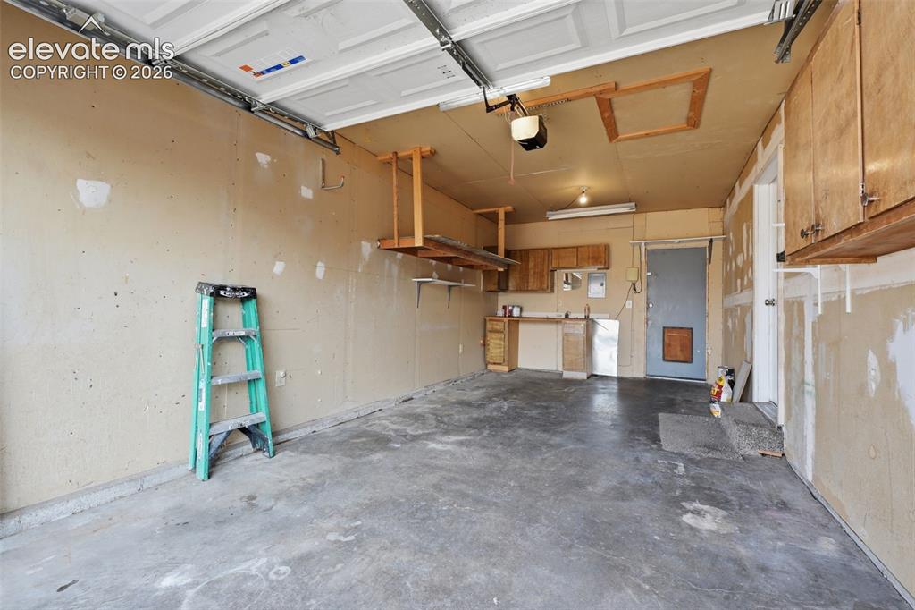 Image 35 of 36: Attached overhead garage door, built-in cabinetry, concrete flooring, utili