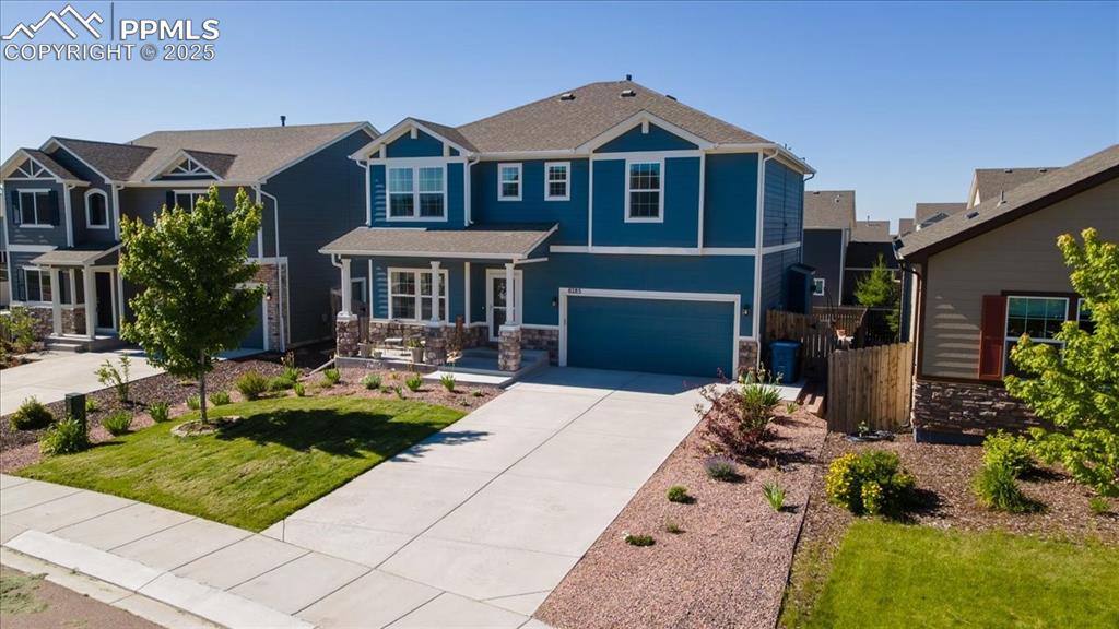 Caption: Craftsman house with an attached garage, concrete driveway, covered porch, and stone siding