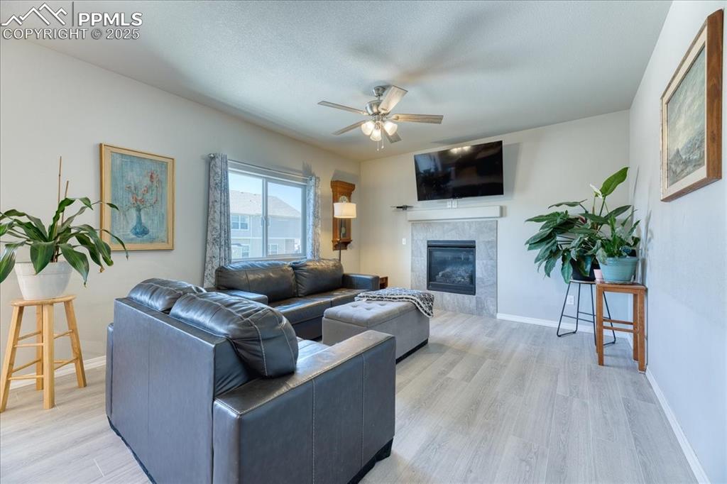 Image 12 of 39: Living room featuring a ceiling fan, a tiled fireplace, and light wood-type