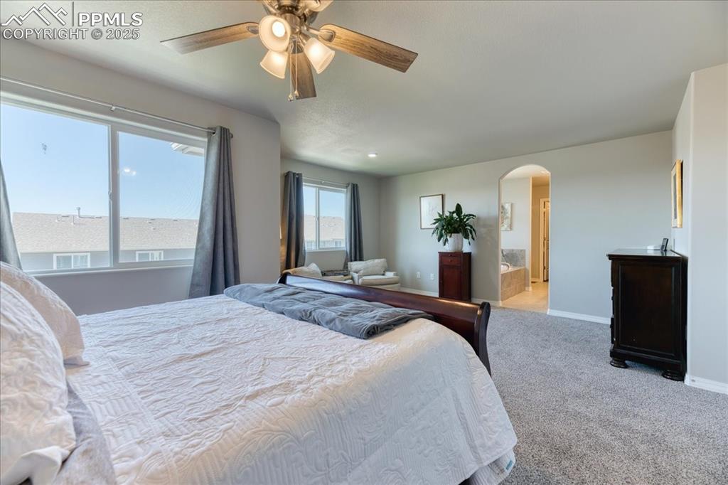 Image 22 of 39: Carpeted bedroom featuring arched walkways, ceiling fan, and ensuite bath