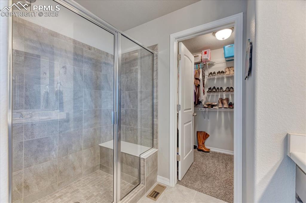 Image 24 of 39: Bathroom featuring a shower stall, a spacious closet, and tile patterned fl