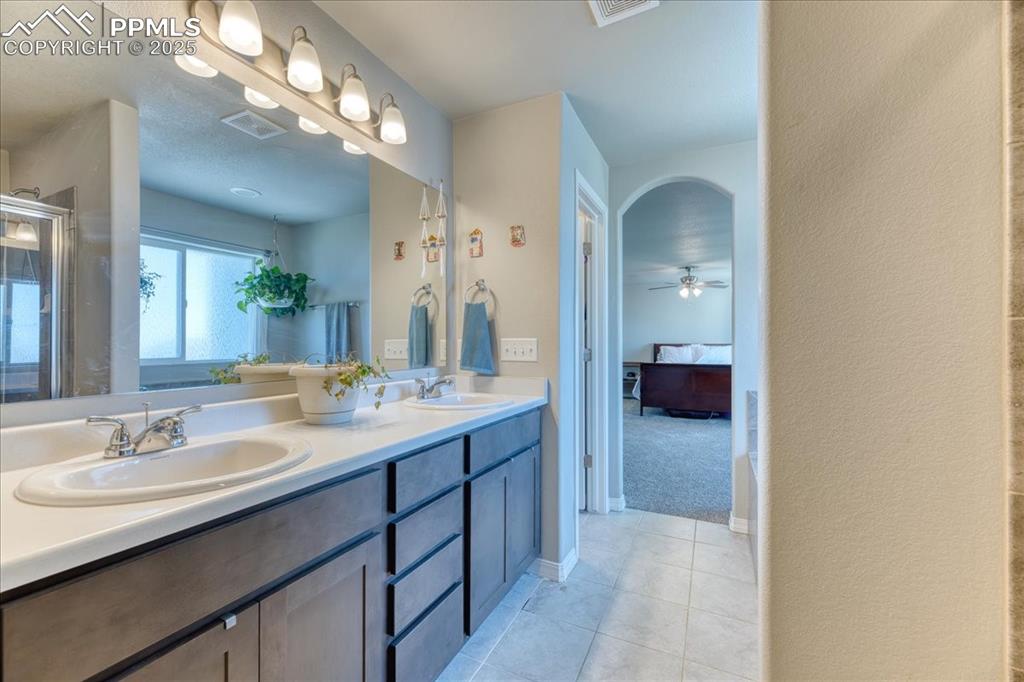 Image 25 of 39: Ensuite bathroom with double vanity, tile patterned floors, ceiling fan, an