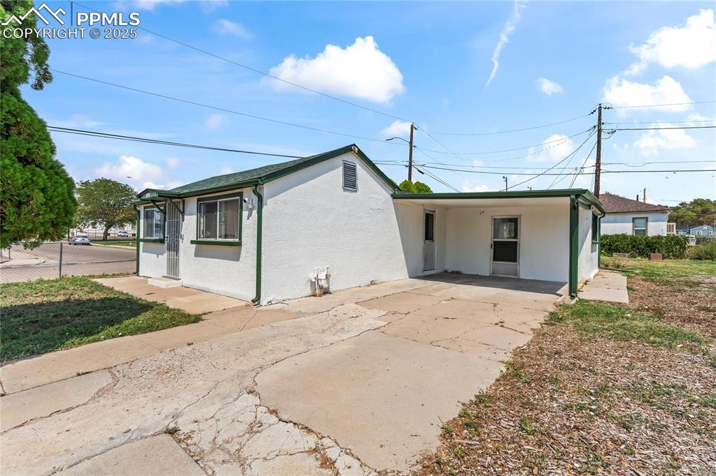 Caption: Back of property with driveway, stucco siding, and an attached carport
